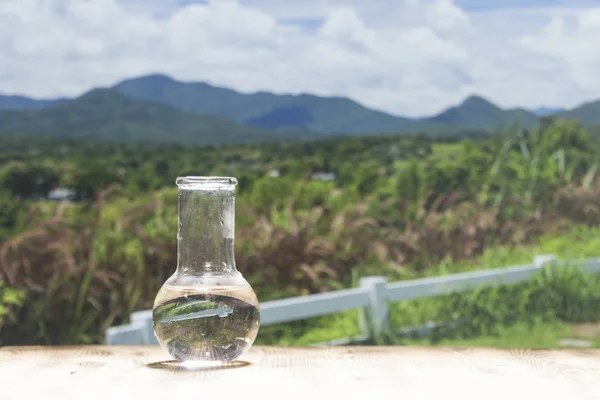 Clean water in a glass laboratory flask on wooden table on mountain background. Ecological concept, the protection of water resources, the test of purity and quality of water.