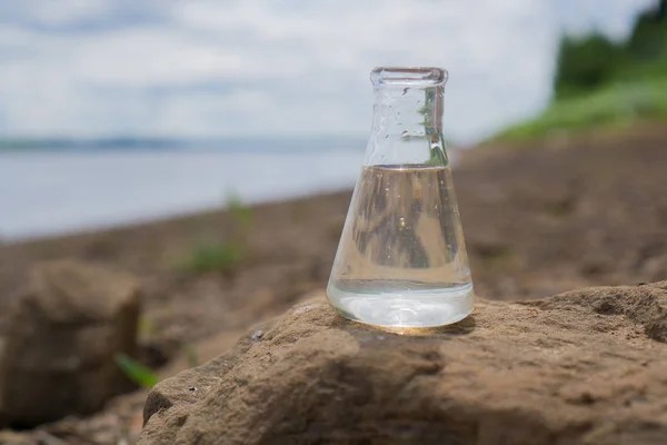 Химическая колба с водой, озером или рекой на заднем плане . — стоковое фото