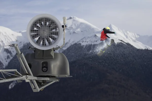 Snökanon i mountain ski resort och flygande snowboardåkare. Stockfoto