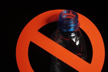 Siyah arka planda dur işareti olan boş mavi plastik şişe. Plastik kirliliğini, geri dönüşüm plastiğini, plastiği durdurma kavramı.
