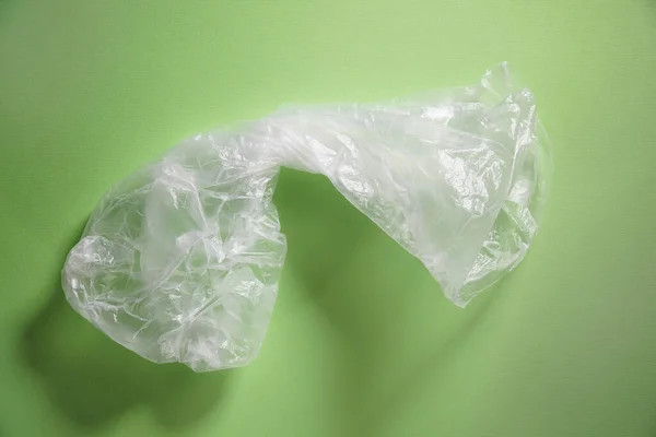 Empty crumpled plastic bag on green background. Concept of plastic pollution, global warming, recycling plastic, plastic free.