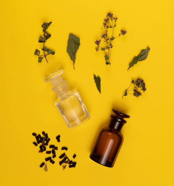 Dos viales vacíos y hojas secas y flores sobre fondo amarillo . — Foto de Stock