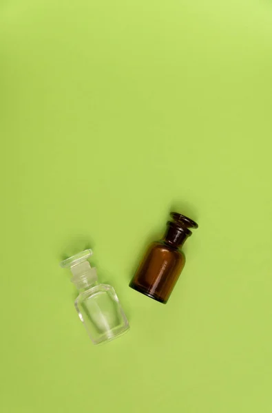 Дві порожні скляні пляшки на зеленому тлі. Парфуми, медицина, хімічний фон . — стокове фото