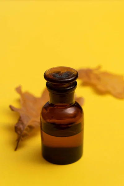 Dry oak leaves and glass bottle on yellow background — 图库照片