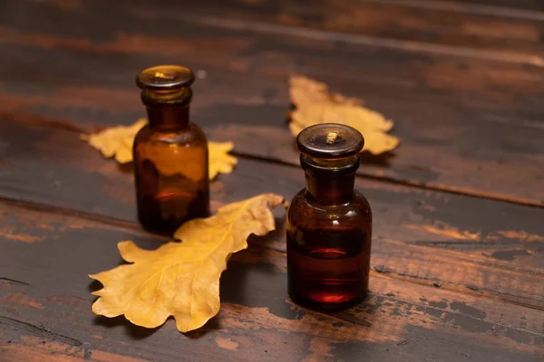 Small bottles on a wooden surface with dried oak tree leaves. Autumn still life composition. — Stock Photo, Image