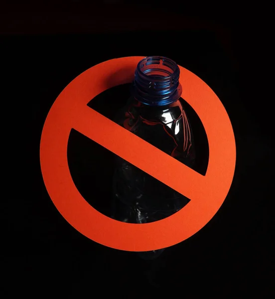 Tomma blå plastflaska i en stoppskylt på svart bakgrund. Begreppet stopp plast förorening, återvinning plast, plast fri. Stockbild