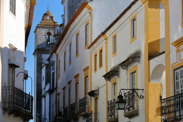 Evora, Portugalsko: typická úzká ulice s bílými domky a kostel Sao Mamede v pozadí — Stock fotografie