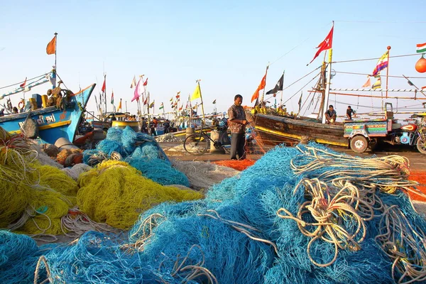 DIU, INDIA - 9 DE ENERO DE 2014: Pescador trabajando en su red en el puerto pesquero de Vanakbara con coloridas redes de pesca en primer plano — Foto de Stock