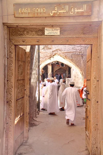 NIZWA, OMÁN - 3 DE FEBRERO DE 2012: Entrada del Zoco Oriental en el casco antiguo de Nizwa con hombres omaníes tradicionalmente vestidos —  Fotos de Stock