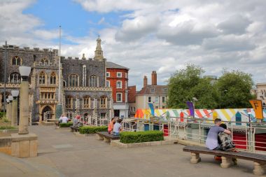 NORWICH, UK - JUNE 4, 2017: People relaxing at Memorial Gardens overlooking colorful market stalls and with the Guildhall in the background clipart