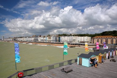 Hastings, İngiltere - 23 Temmuz 2017: Sahil ile ön ve güzel bir bulutlu gökyüzü renkli kulübelerde iskelesinden (yeniden inşa edildi ve 2016 yılında halka açık) görünümünü