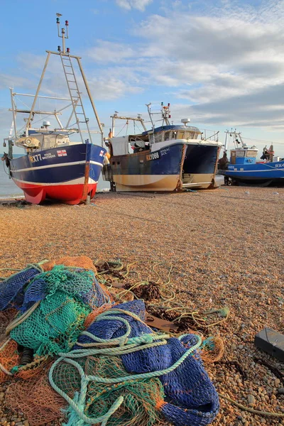 Hastings, Velká Británie - 21. července 2017: Beach zahájila rybářské lodě při západu slunce s barevnými rybářskými sítěmi v popředí — Stock fotografie