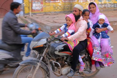 BUNDI, RAJASTHAN, INDIA - DECEMBER 10, 2017: Local transport with a smiling family travelling on a motorcycle in the streets of the old town clipart