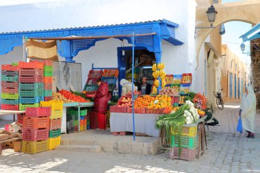 Kairouan, Tunus - 12 Aralık 2019: Medine 'nin içinde geleneksel olarak beyaz giyinmiş bir kadının bulunduğu geleneksel bir meyve ve sebze dükkanı