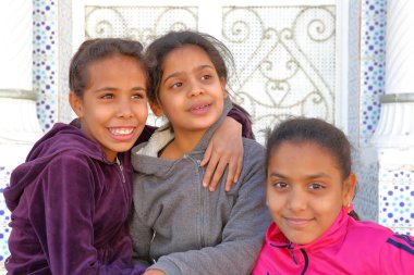 TOZEUR, TUNISIA - DECEMBER 20, 2019: portrait of three smiling little girls in Tozeur, with a traditional door in the background