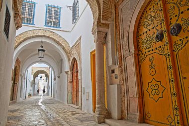 Typical cobbled and narrow street with colorful doors, columns and arcades inside the historical medina of Tunis, Tunisia clipart