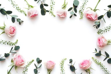 Beyaz arka planda pembe güllerden ve yeşil yapraklardan yapılmış bir çerçeve. Yukarıdan bak. Boşluğu kopyala.