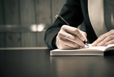 Close up of business people hand in suit writing on notebook or  clipart