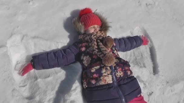 Mädchen macht einen Schmetterling im Schnee, Winterwetter — Stockvideo