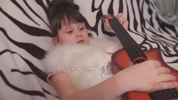 Девушка лжет и играет на детской гитаре — стоковое видео