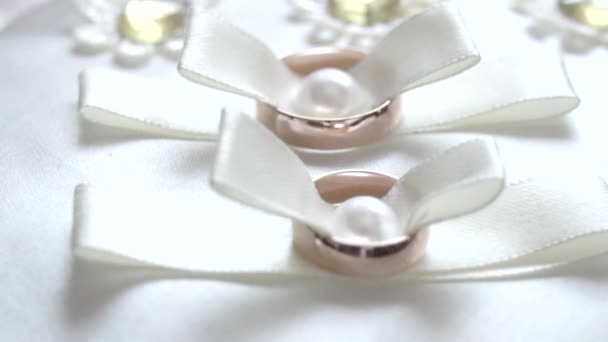 Svatební prsteny na bílém polštáři. Koncept svatebních událostí - dva zlaté prsteny na luku z modré stuhy. — Stock video