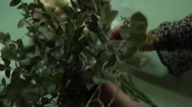 Bir çiçekçi bir kadında doğal sisal esaslı bir buket toplar. Floristik bir profesyonel bir çerçeve yeşil yapraklarla dolu özel malzeme tutar. Kırmızı manikür ile master