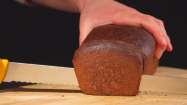 Ağır çekimde ahşap tahta üzerinde dilim ekmek kestim. Erkek el ahşap masanın üzerine ev yapımı ekmek dilimleme. 