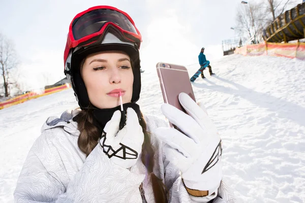 Female snowboarder applying lip gloss — Stock Photo