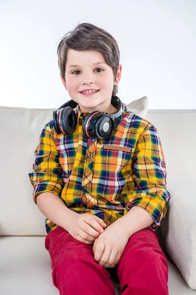 Chlapec se sluchátky na uších sedí na pohovce — Stock fotografie