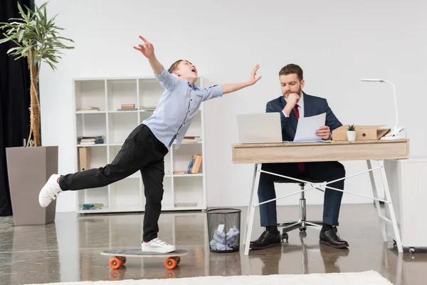 Boy skateboarding while father working — Stock Photo, Image