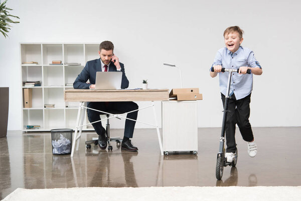 Счастливый мальчик катается на скутере в офисе
