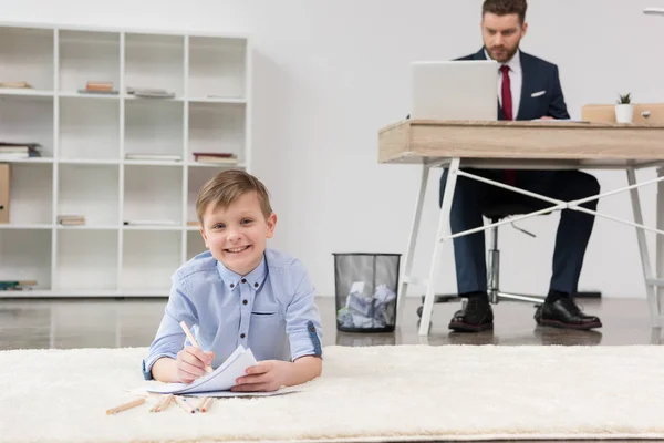 Boy drawing while his father working — Stock Photo