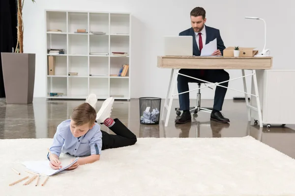 Boy drawing while his father working — Stock Photo