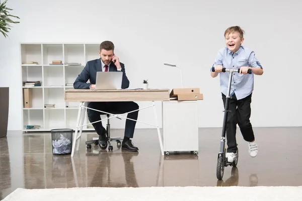 Niño feliz montando skooter en la oficina - foto de stock