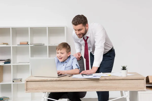 Businessman playing on laptop with son — Stock Photo