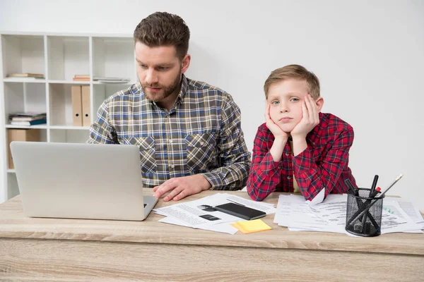 Freelancer trabajando en la mesa con su hijo - foto de stock