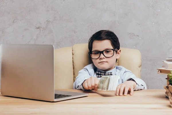 Criança com dinheiro no local de trabalho com laptop — Fotografia de Stock