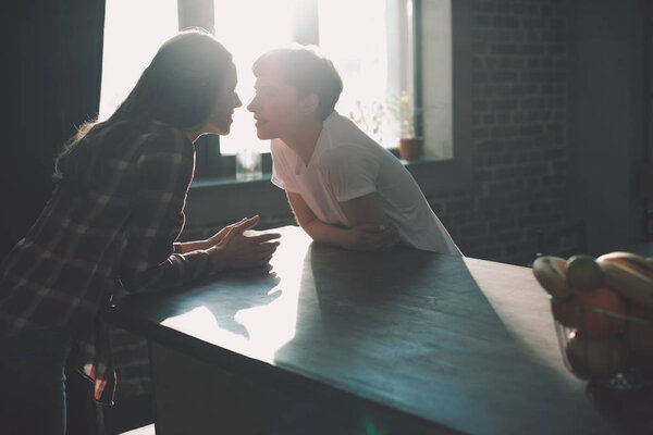 silhouettes of young lesbian couple spending time together and kissing on kitchen in morning