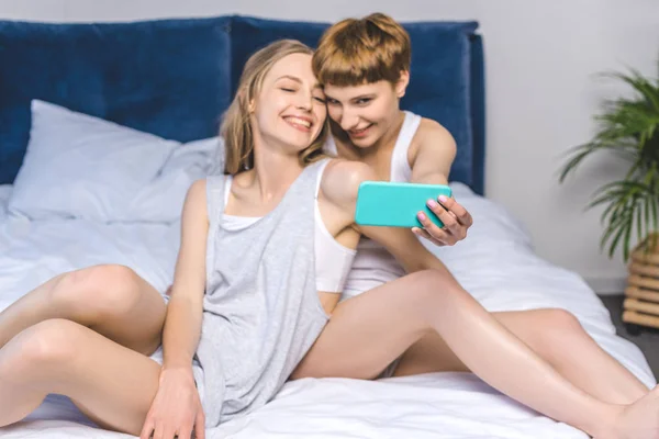 Young Lesbian Couple Taking Selfie While Sitting Bed Stock Photo