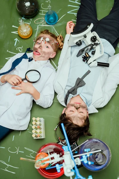 Kids in lab coats lying on chalkboard — Stock Photo