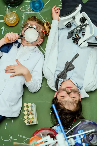 Niños en batas de laboratorio acostados en pizarra - foto de stock