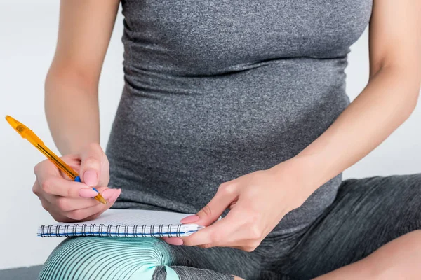 Pregnant woman writing in notepad — Stock Photo