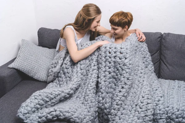 Heureux jeune couple lesbien sous couverture de laine tricotée sur canapé — Photo de stock