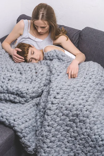 Young lesbian couple spending time together under knitted wool blanket on couch — Stock Photo