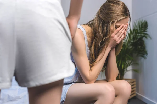 Young woman sitting on bed and crying while her girlfriend standing on foreground — Stock Photo