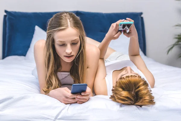 Junges lesbisches Paar vernetzt sich im Bett mit Smartphones — Stockfoto