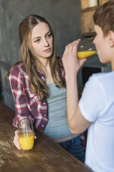 Молодые женщины пьют свежий апельсиновый сок на кухне — стоковое фото