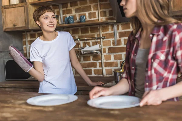 Giovani donne felici rendendo la tavola apparecchiata per la cena in cucina — Foto stock