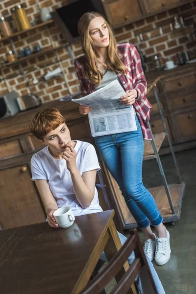 Молодые привлекательные женщины читают газеты и пьют кофе на кухне утром — стоковое фото