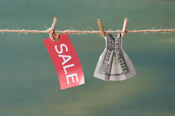 знак продажи и долларовая купюра на бельевой веревке
